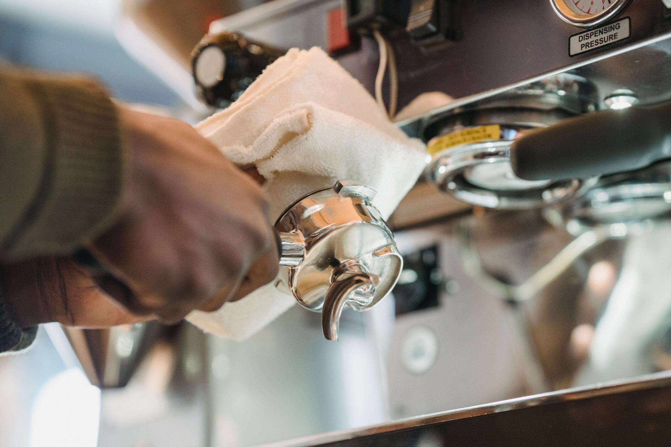 Home Close-up of barista cleaning a coffee machine portafilter with cloth for hygiene.